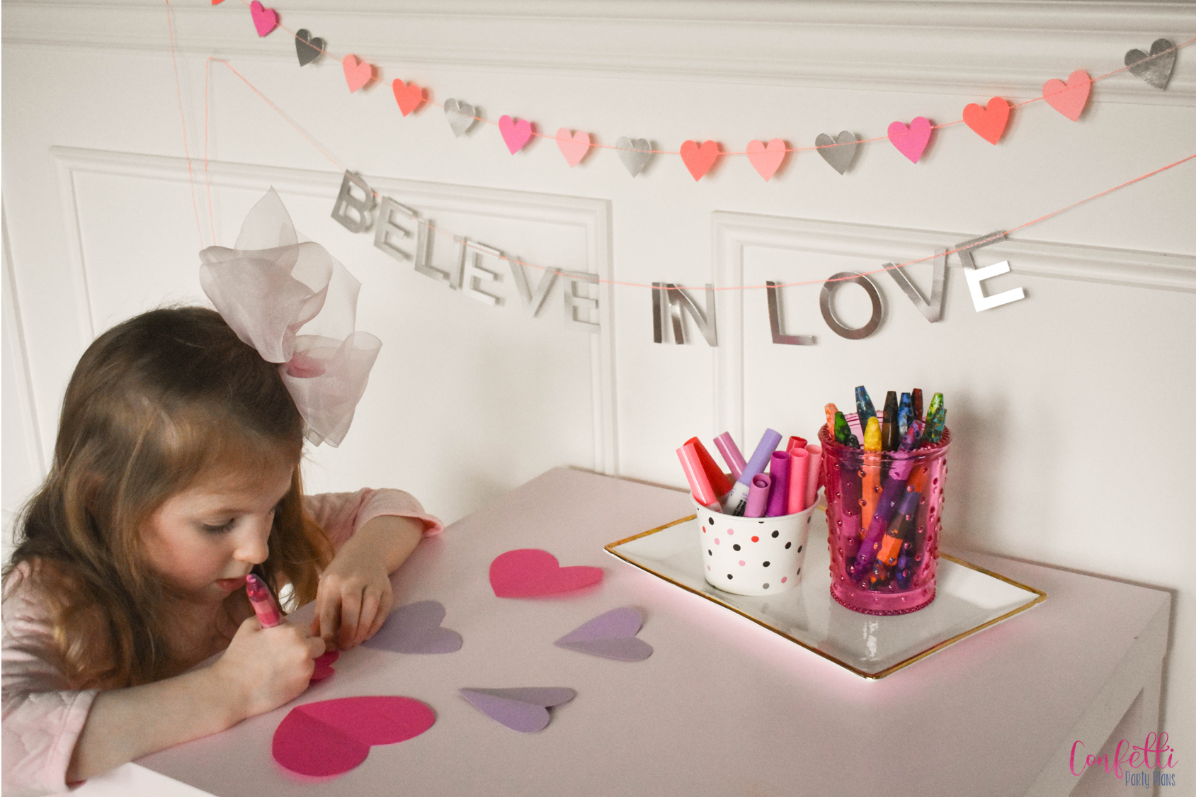 little girl in pink bow coloring on pink and purple hearts