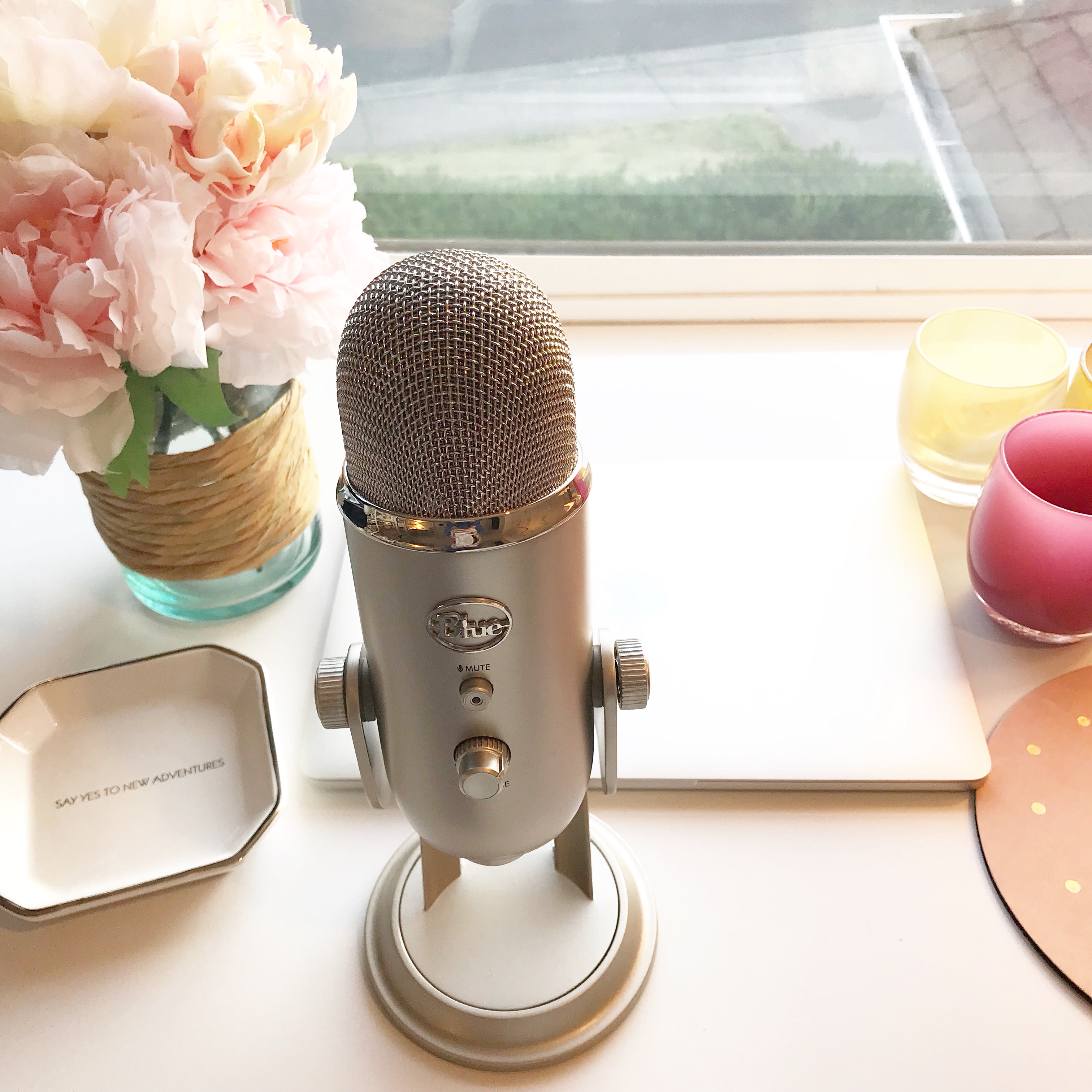 podcast microphone on a desk with laptop and vase of flowers