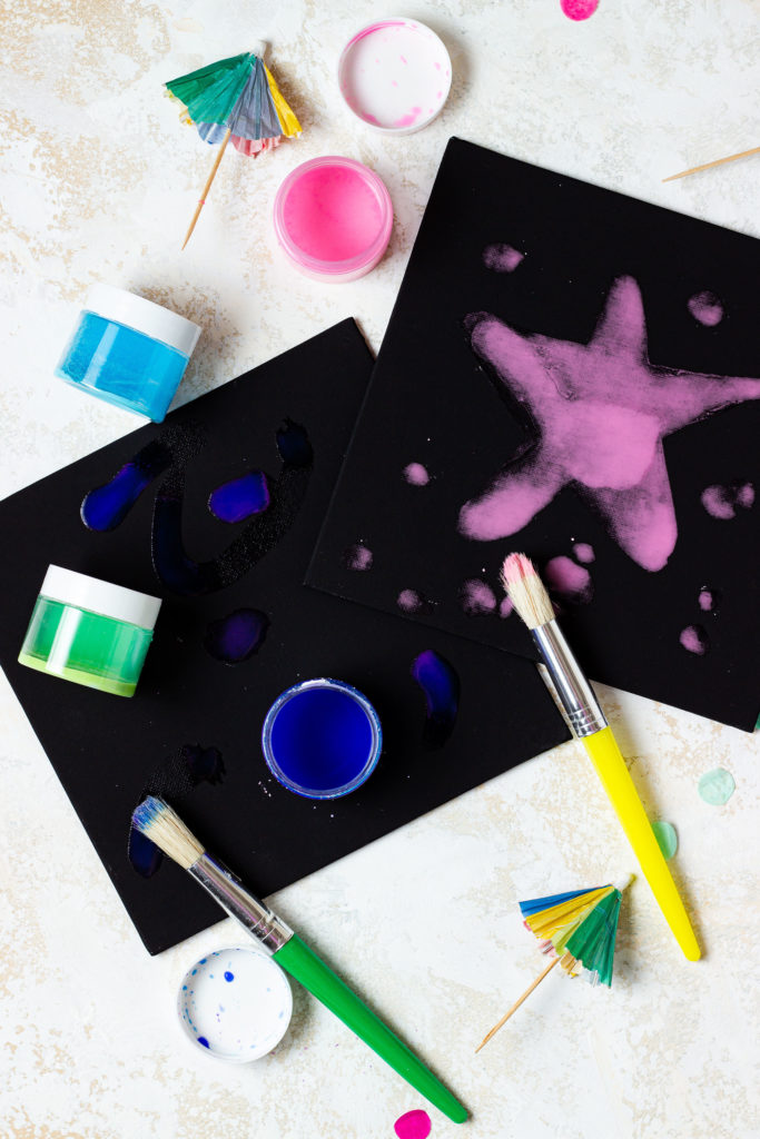 pink and blue sidewalk chalk painted on a black board with a paintbrush as an activity included in a Memories in Moments Unwrapped box filled with summer themed crafts and activities for kids and busy moms to survive summer break at home