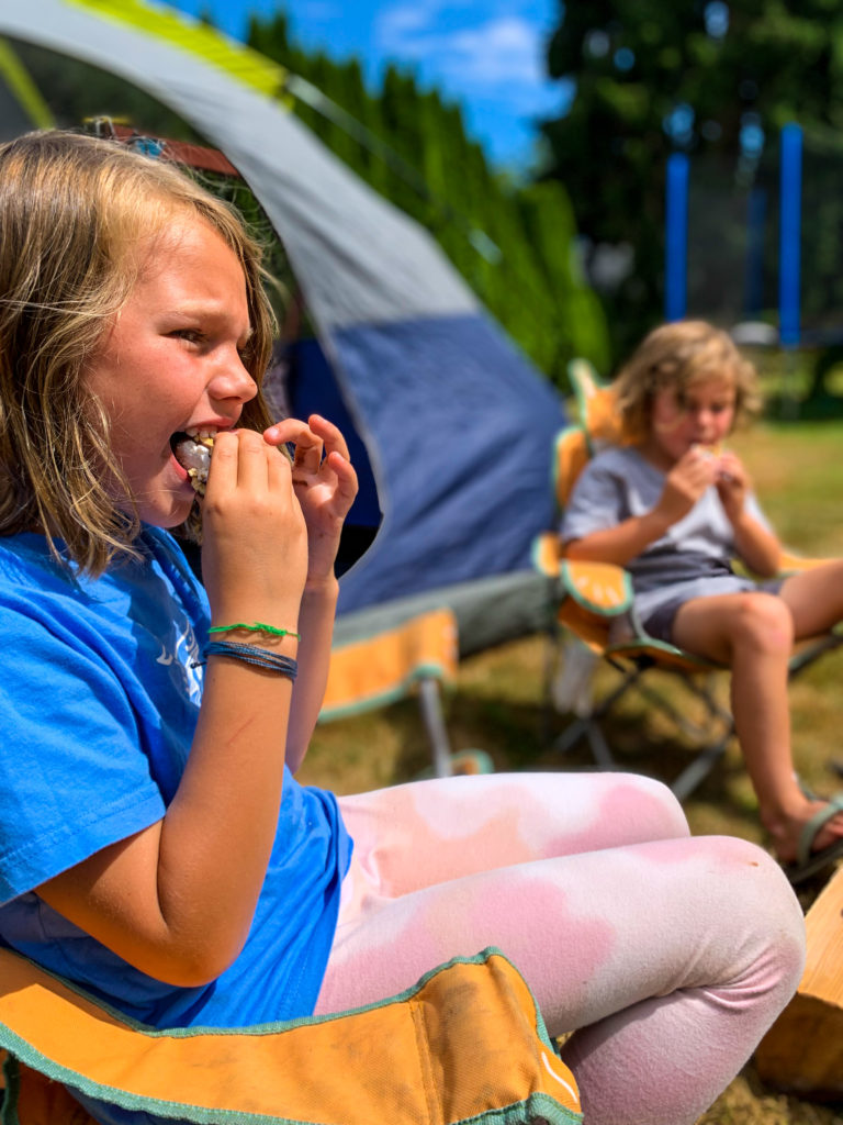 kids eating smores in backyard by tent - Travel blogger Nikki Harrington shares seven ideas that will turn your backyard into the ultimate (easy) family camping adventure!